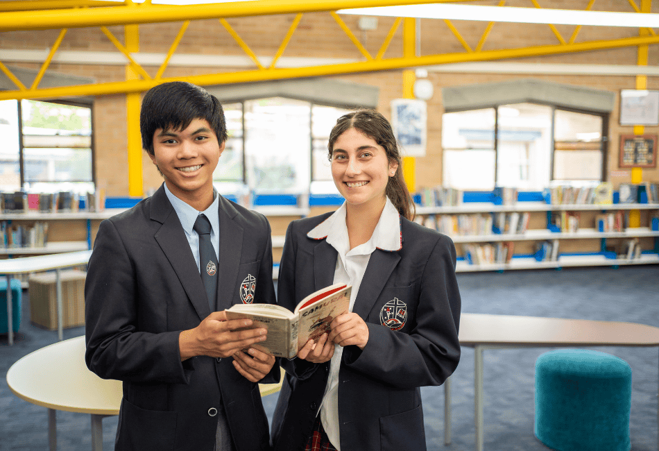 A photo of two secondary students sharing a book and smiling 